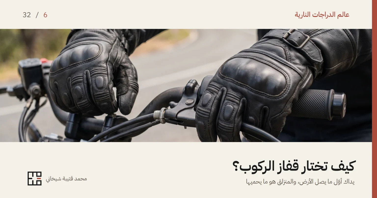 يدا درّاج بقفازين جلديين أسودين على مقود دراجة نارية، تظهر عليهما دروع بارزة فوق مفاصل الأصابع ودروع أصغر على السلاميات، وحزام إغلاق بإبزيم عند المعصم.