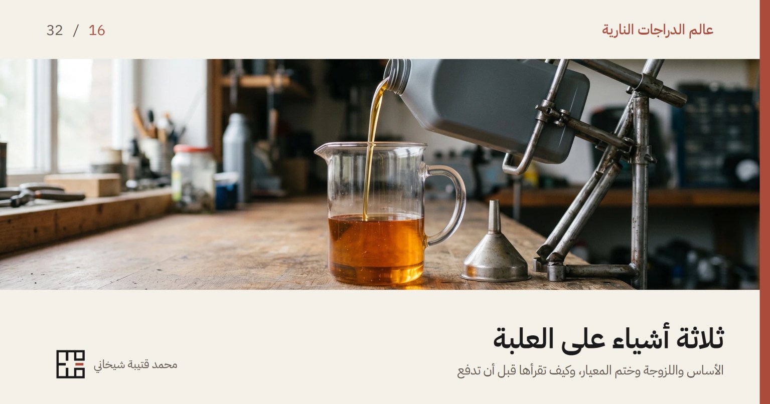 غلاف مقال زيت محرك الدراجة النارية: إبريق زجاجي شفّاف على طاولة عمل خشبية نصفه مملوء بزيت محرّك كهرمانيّ يمرّ فيه الضوء، وفوقه زجاجة زيت رمادية بلا ملصق مائلة في حمّالة فولاذية تصبّ خيطاً رفيعاً من الزيت في الإبريق، وإلى جانبه قمع معدني صغير، وخلفهما رفوف ورشة خارج التركيز.
