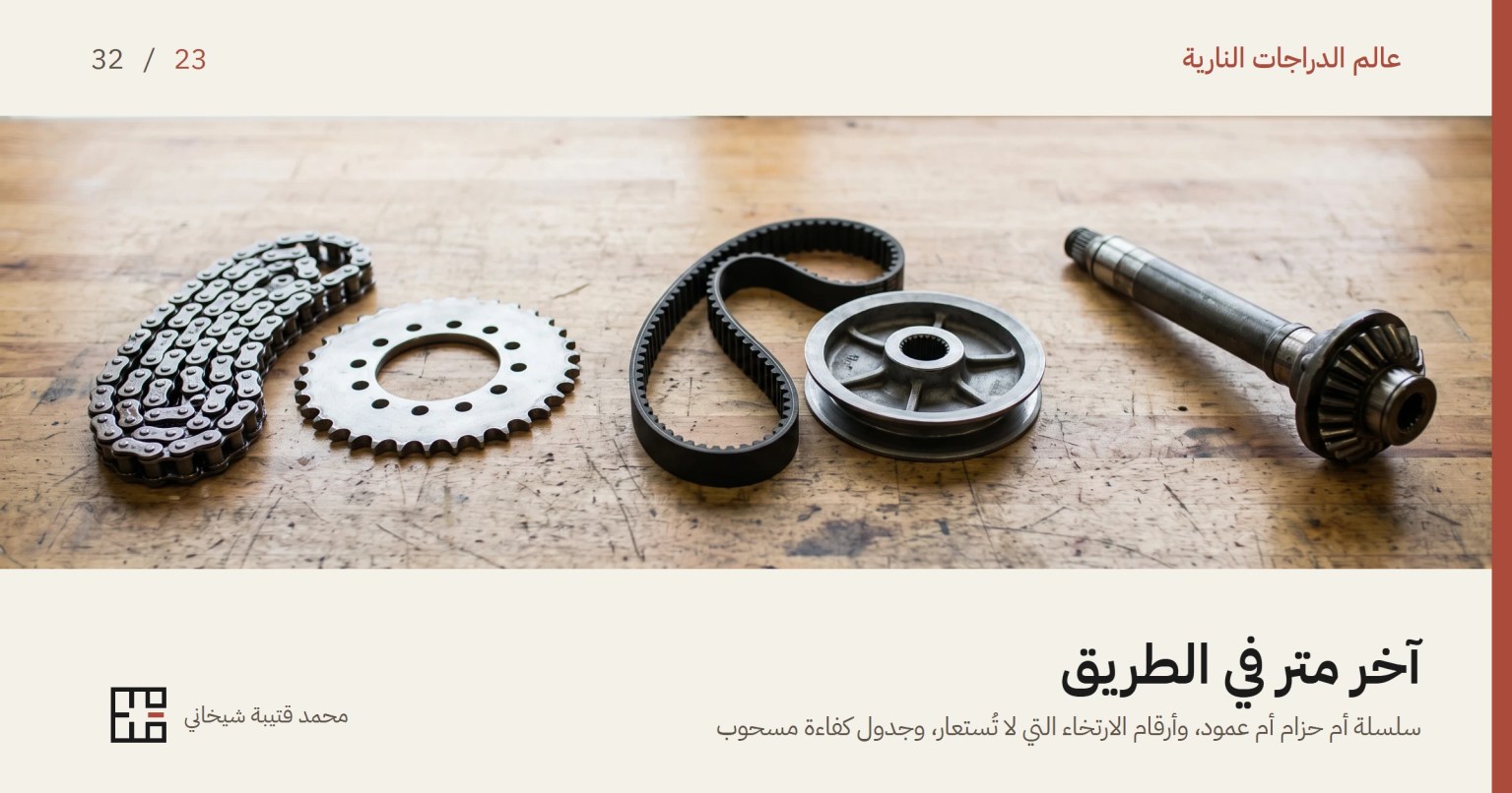 غلاف مقال نظام الدفع النهائي للدراجة النارية: سلسلة وترس خلفي وحزام مسنَّن وبكرته وعمود إدارة بترسه المخروطيّ، مفروشة بالترتيب على طاولة ورشة خشبية قديمة أمام نافذة.