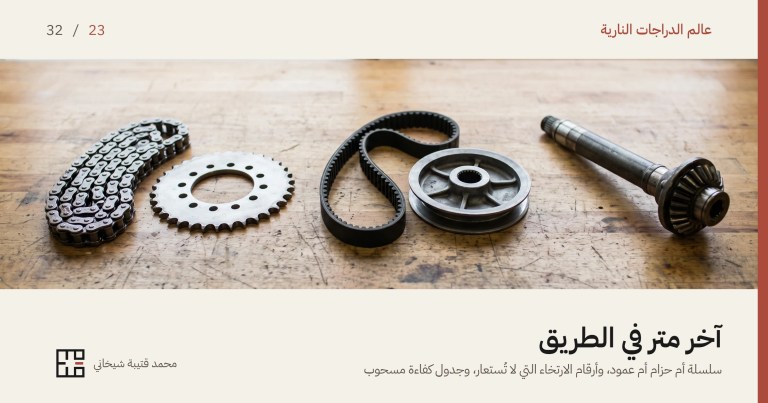 غلاف مقال نظام الدفع النهائي للدراجة النارية: سلسلة وترس خلفي وحزام مسنَّن وبكرته وعمود إدارة بترسه المخروطيّ، مفروشة بالترتيب على طاولة ورشة خشبية قديمة أمام نافذة.