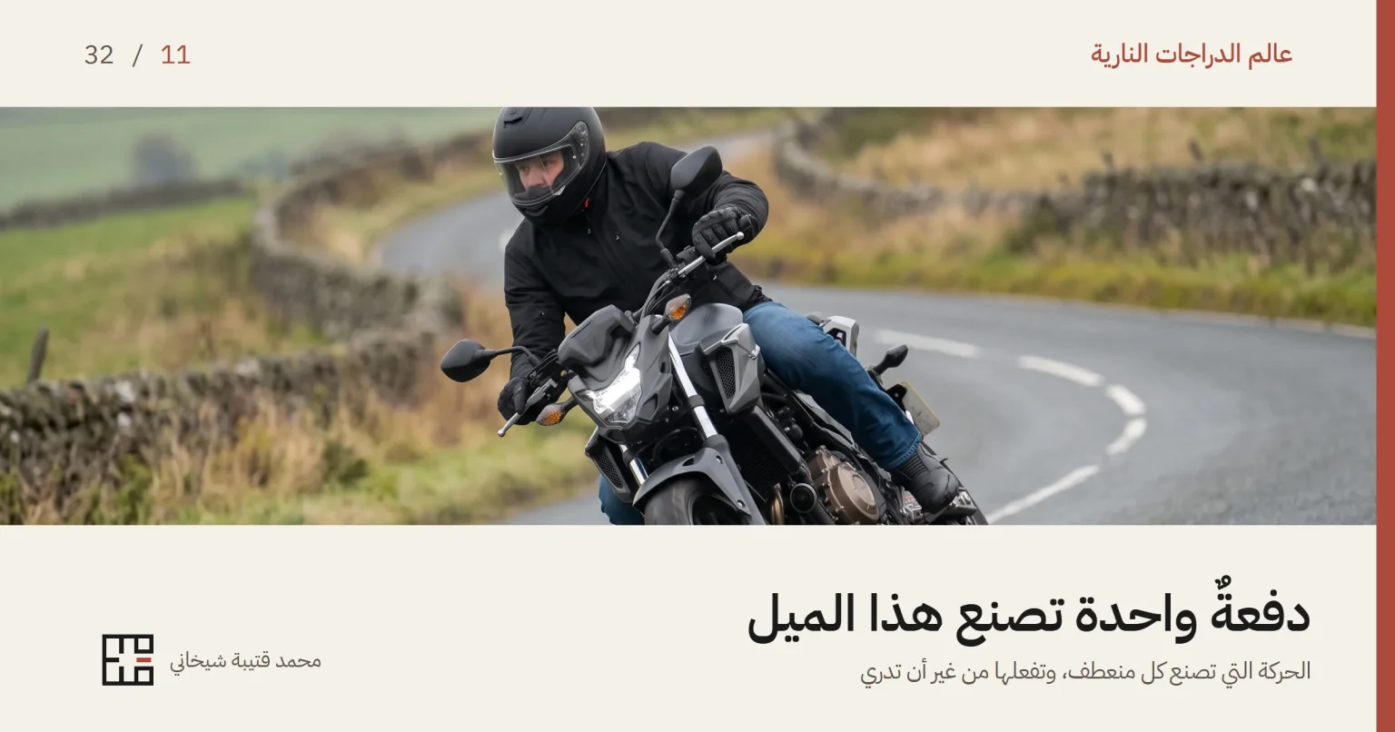 درّاج يقود دراجةً نارية عارية متوسّطة السعة في منعطفٍ على طريق ريفيّ، والدراجة مائلة إلى داخل المنعطف ويداه مطبقتان على مقبضَي المقود. يرتدي خوذةً كاملة الوجه سوداء مطفأة وجاكيتاً قماشياً أسود، وخلفه جدارٌ حجريّ جافّ ومروجٌ خضراء في يوم غائم.